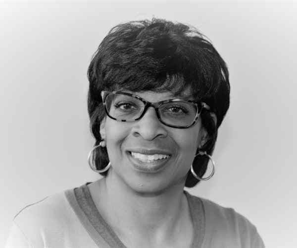 Linda Brooks, smiling, in glasses and hoop earrings