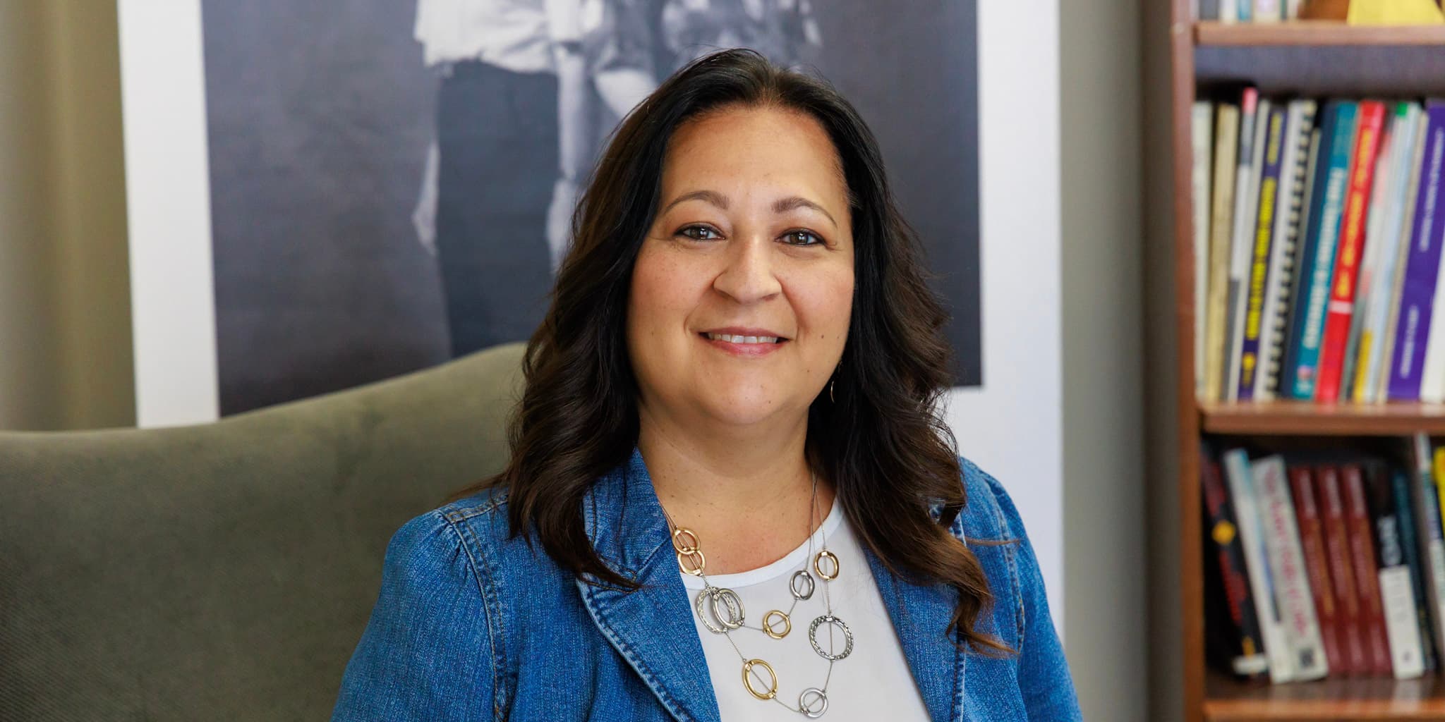 Melissa Palacio in the AdvocacyDenver office, with bookshelves and a black-and-white photo mural behind her